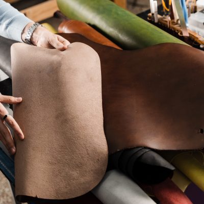 Leather craftsman is touching roll of genuine leather in the workshop. Rolls of genuine leather of different colors in leather products workshop